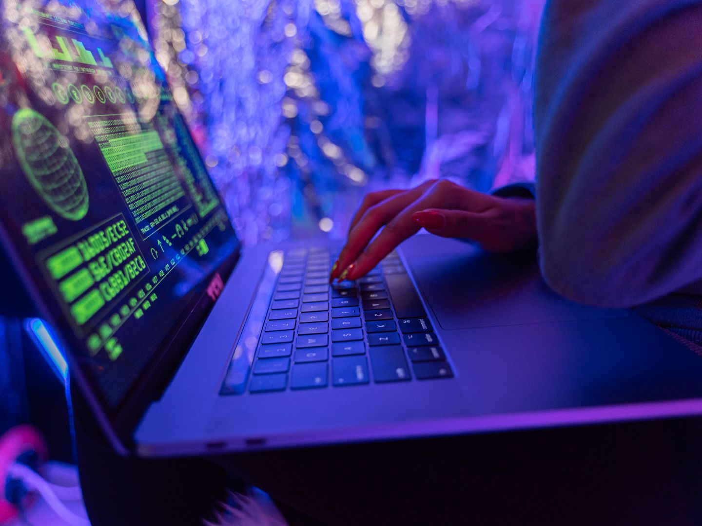 Close up of hands typing on a laptop displaying cybersecurity graphics, illuminated by purple light.