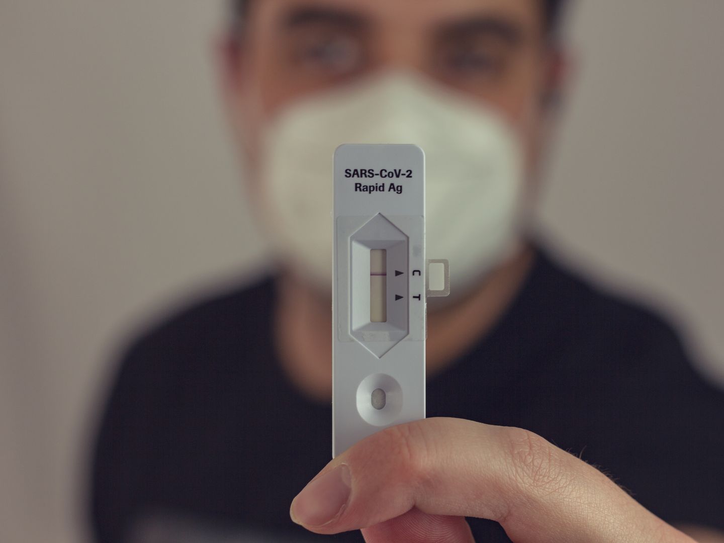 A person holding a negative COVID 19 antigen test with a face mask on, focused on the test result.